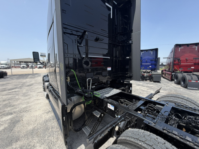 Truck chassis and cab area showing rear of Mack PR64T76H with chassis rails, fuel lines, and connection points; visible area includes rear of cab and front frame with steps and wiring harness.