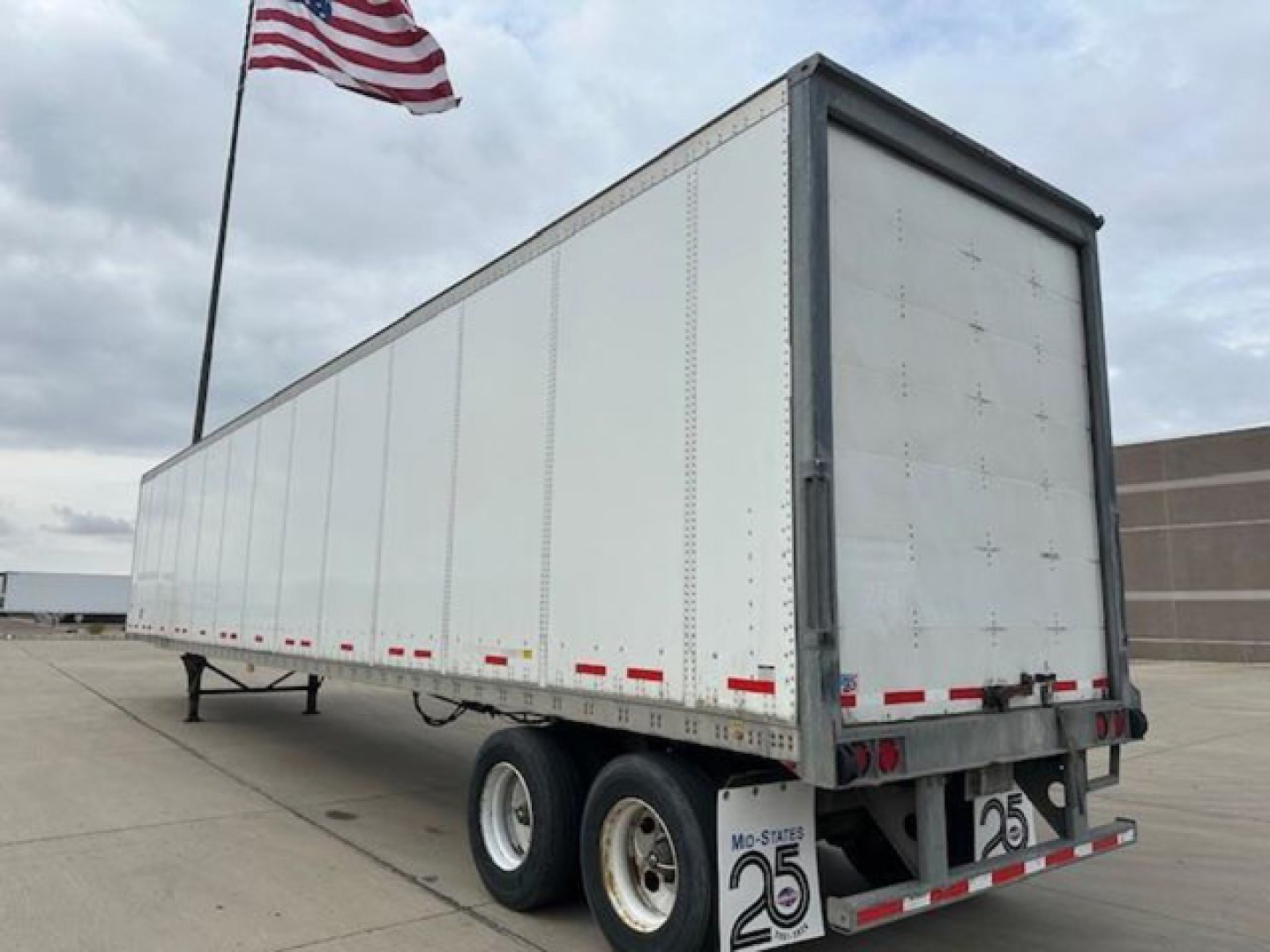 Trailer: 2014 Wabash van trailer in side view showing double rear wheels and tandem axle, with license plate bracket and MO-States 25 sticker, U.S. flag in background.