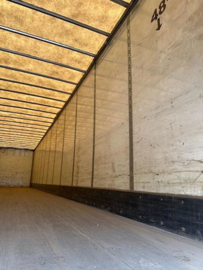 Van trailer interior with wooden floor and white insulated walls, empty cargo space, side panels numbered 48'.