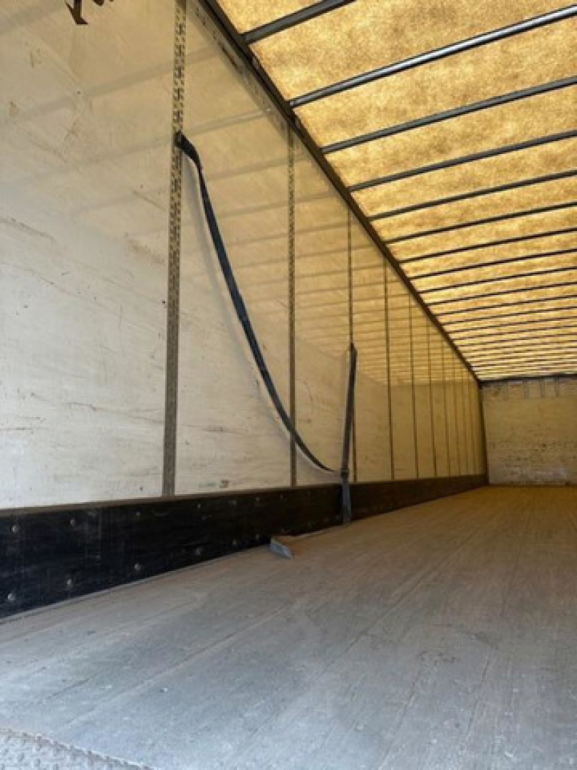 Trailer interior showing sidewall ribs and flooring; black flexible conduit/strap along left wall and overhead beams visible.