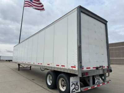 Trailer: 2014 Wabash van trailer in side view showing double rear wheels and tandem axle, with license plate bracket and MO-States 25 sticker, U.S. flag in background.