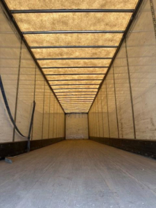 Trailer interior showing long, empty Wabash van trailer with light tan walls, metal ribs, and a wooden floor; perspective down the cargo area.