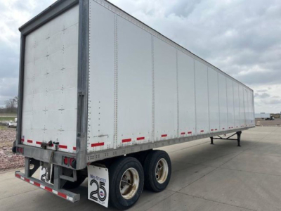 Trailer side view showing a long silver Wabash van trailer with dual rear wheels, rear doors, and red reflective tape along bottom edge; no legible text visible on the container itself.