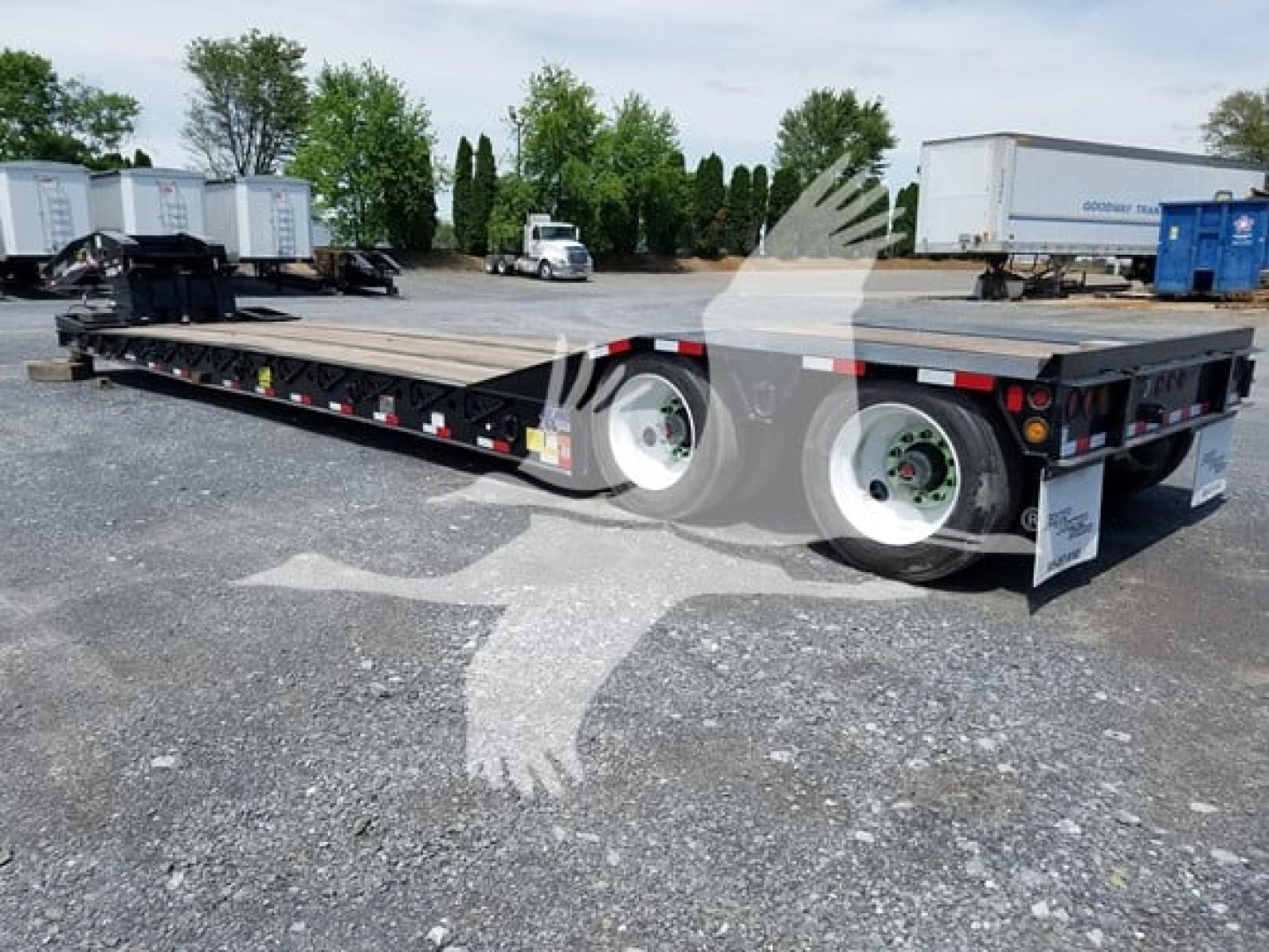 Flatbed trailer with dual rear axles and metal deck, black frame, white wheels, and reflective tape.