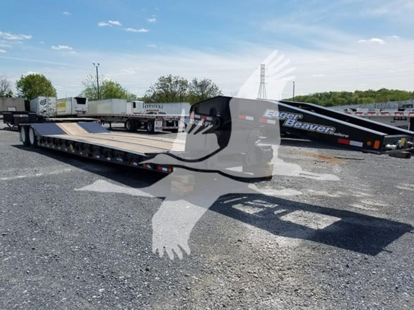 Trailer with lowboy flatbed showing 'Eager Beaver' branding on the gooseneck area and the long deck; clear sky, gravel lot.