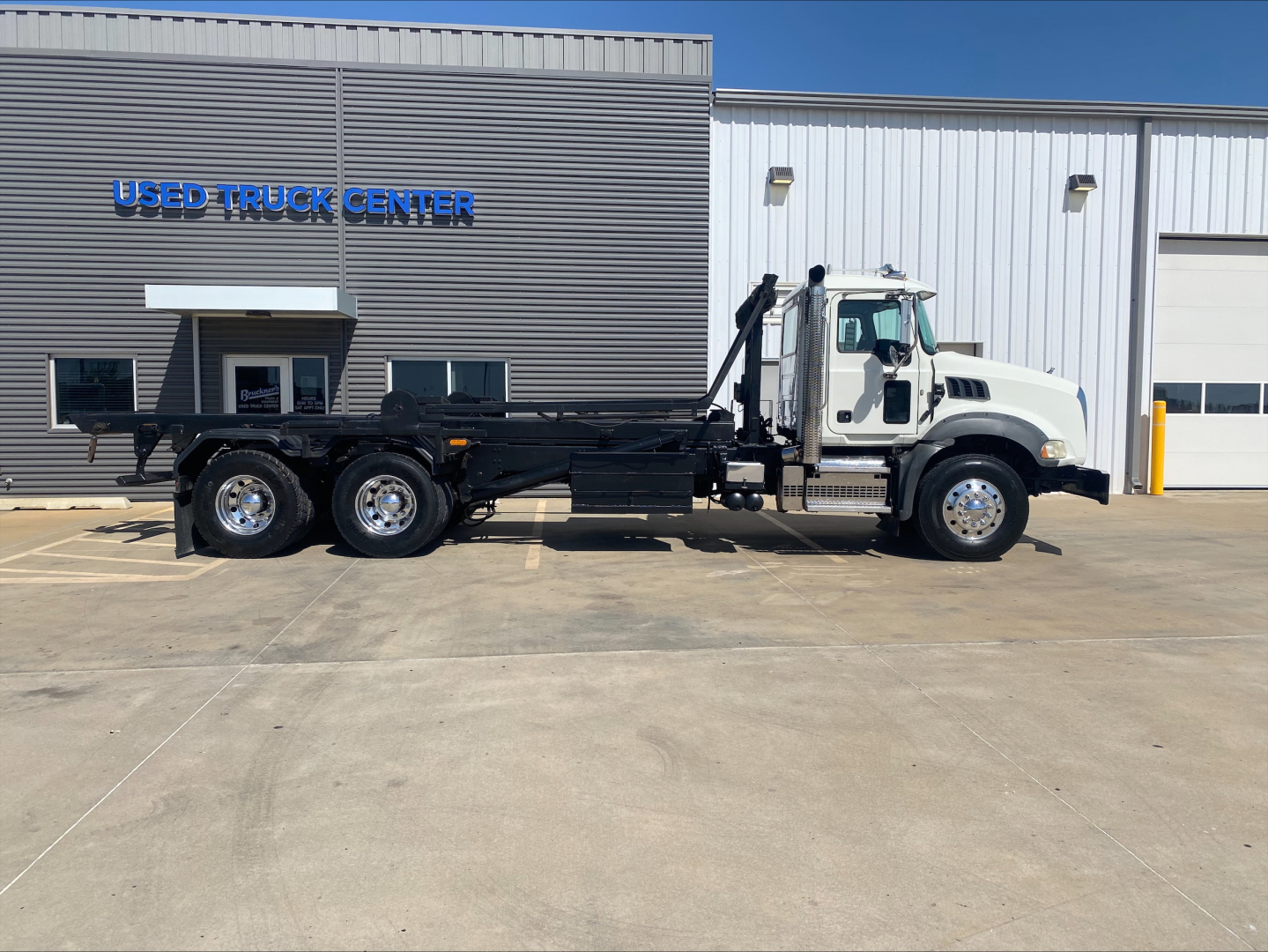 Mack GU533 truck chassis in side view with roll-off body, white cab, black undercarriage, stock number B3199P visible at Used Truck Center
