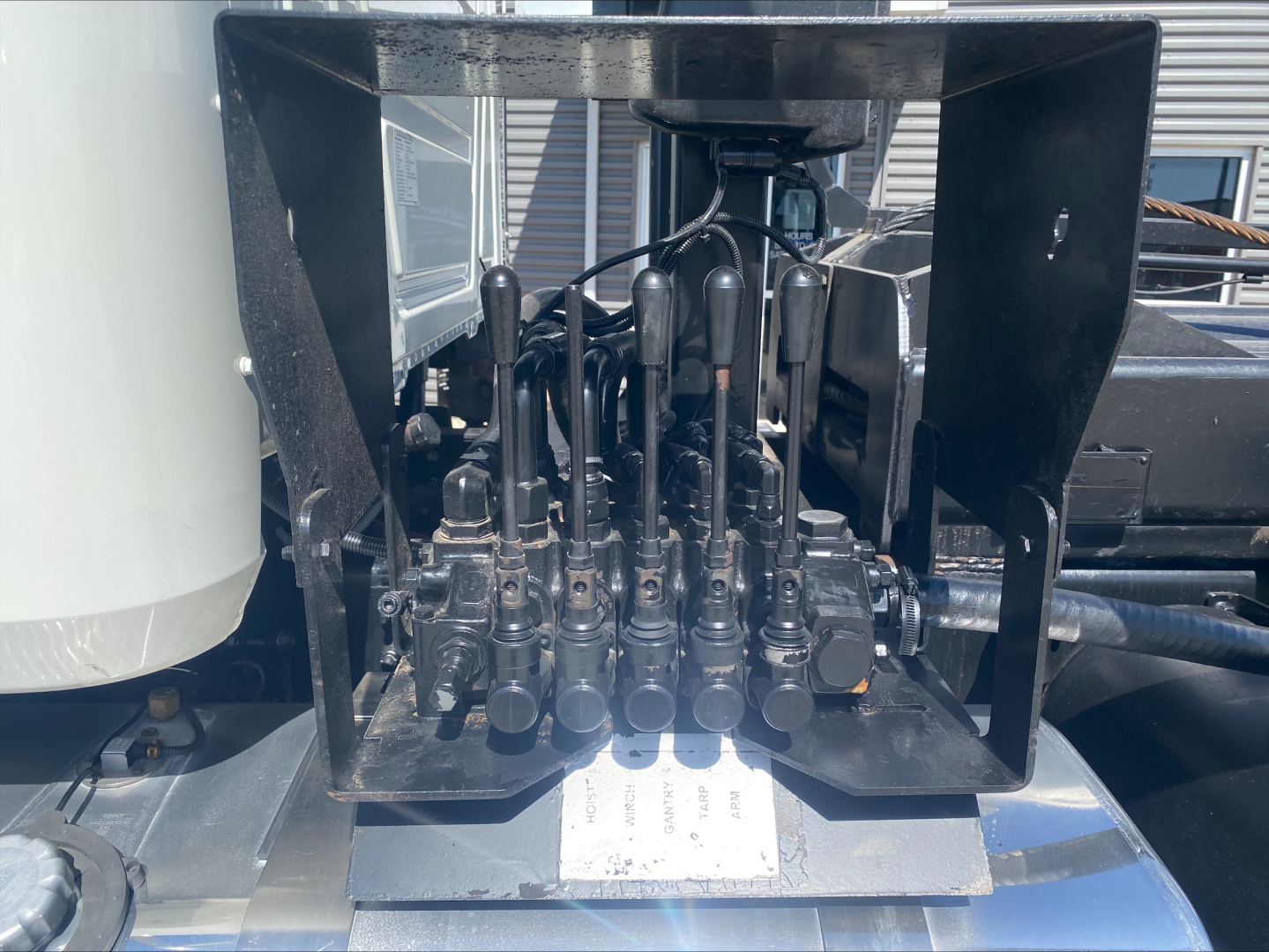 Mack GU533 control valve levers and hydraulic manifold block visible in a truck bed, with multiple black levers and cables inside a metal frame.