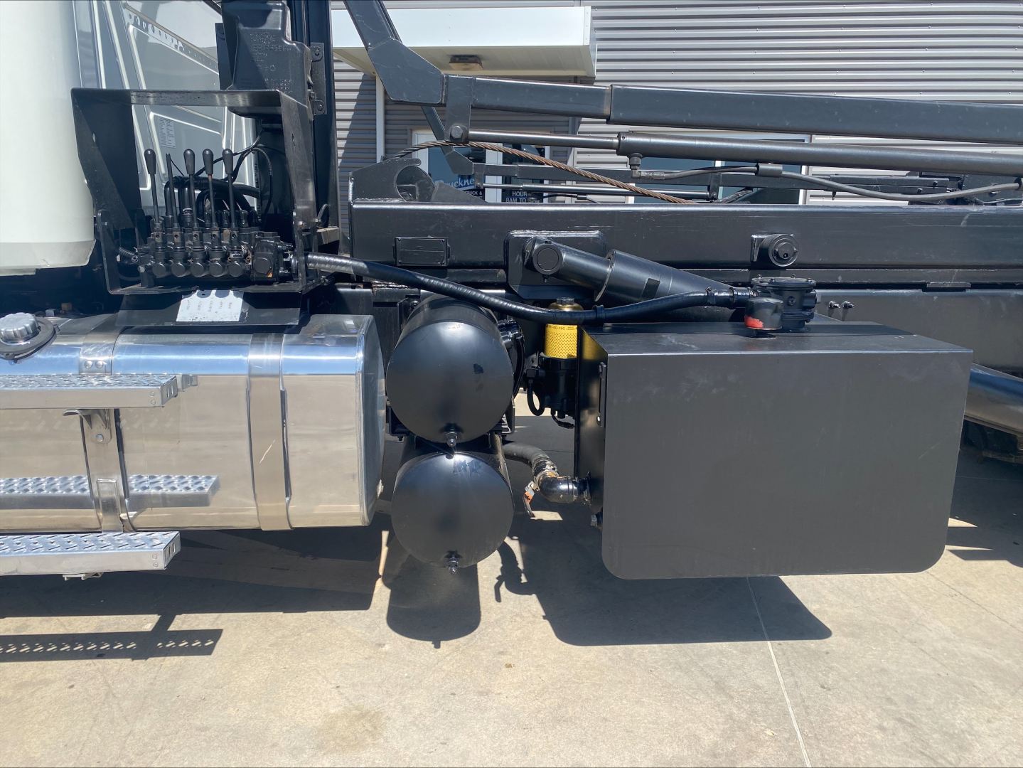 Mack GU533 truck side showing storage tanks and hydraulic components with black square toolbox and chrome fuel tank area.