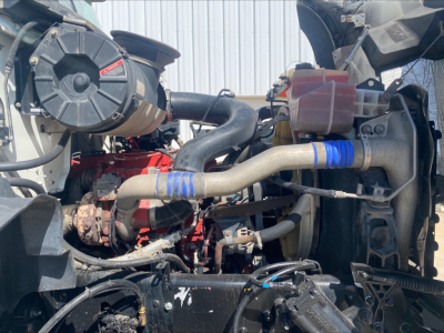 Engine bay of a 2016 Mack GU533 roll-off truck showing large intercooler pipe, radiator, intake hoses, and engine components.