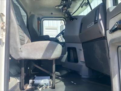 Cab interior of a 2016 Mack GU533 roll-off truck showing driver seat, steering wheel, dashboard, and pedals.