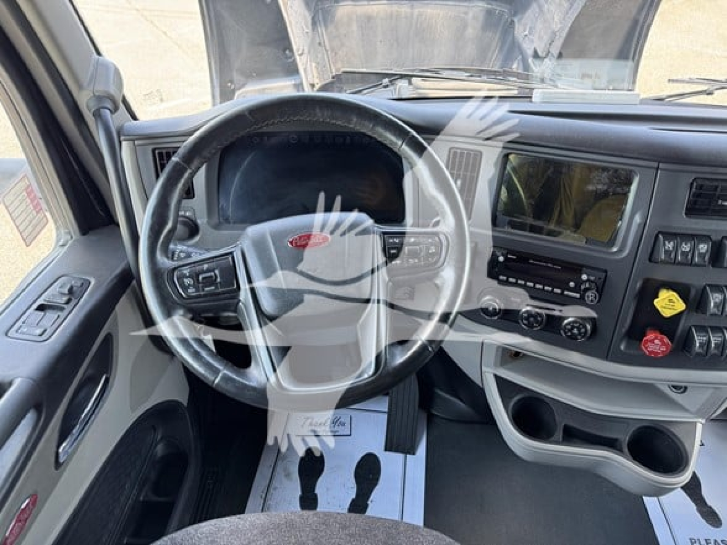 Peterbilt 579 interior dashboard with steering wheel, center console, and instrument cluster; visible text includes Peterbilt logo on steering wheel, radio/climate controls, cup holders, and yellow and red knobs.