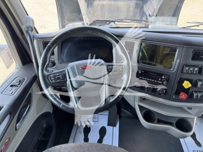 Peterbilt 579 interior dashboard with steering wheel, center console, and instrument cluster; visible text includes Peterbilt logo on steering wheel, radio/climate controls, cup holders, and yellow and red knobs.