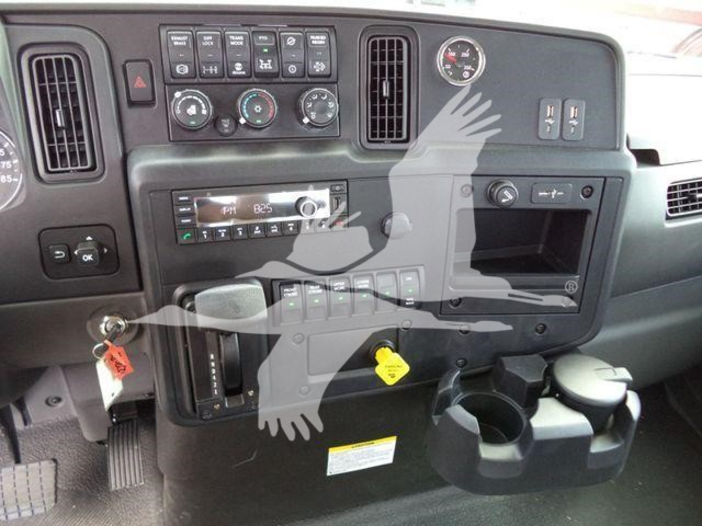 Dashboard of a truck with controls, vents, and cup holders visible. Various gauges and knobs, including climate controls, radio, and warning stickers.