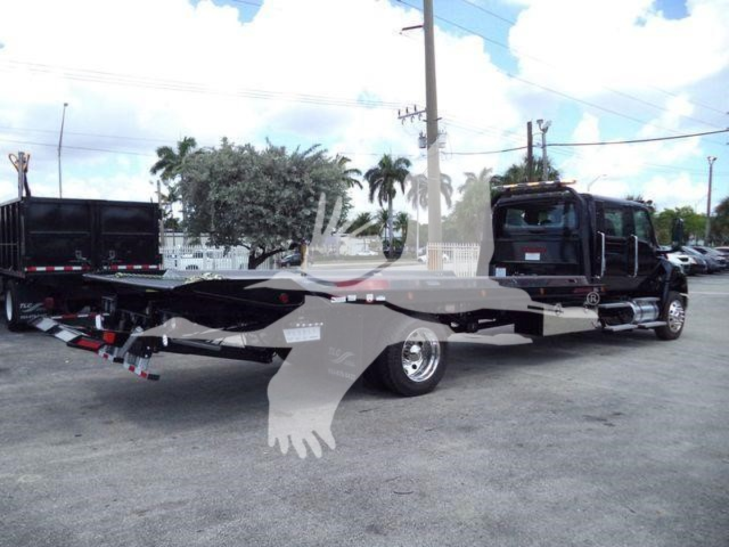 Large tow truck with flatbed rollback in black and silver, International MV model, side view showing extended bed and towing equipment.