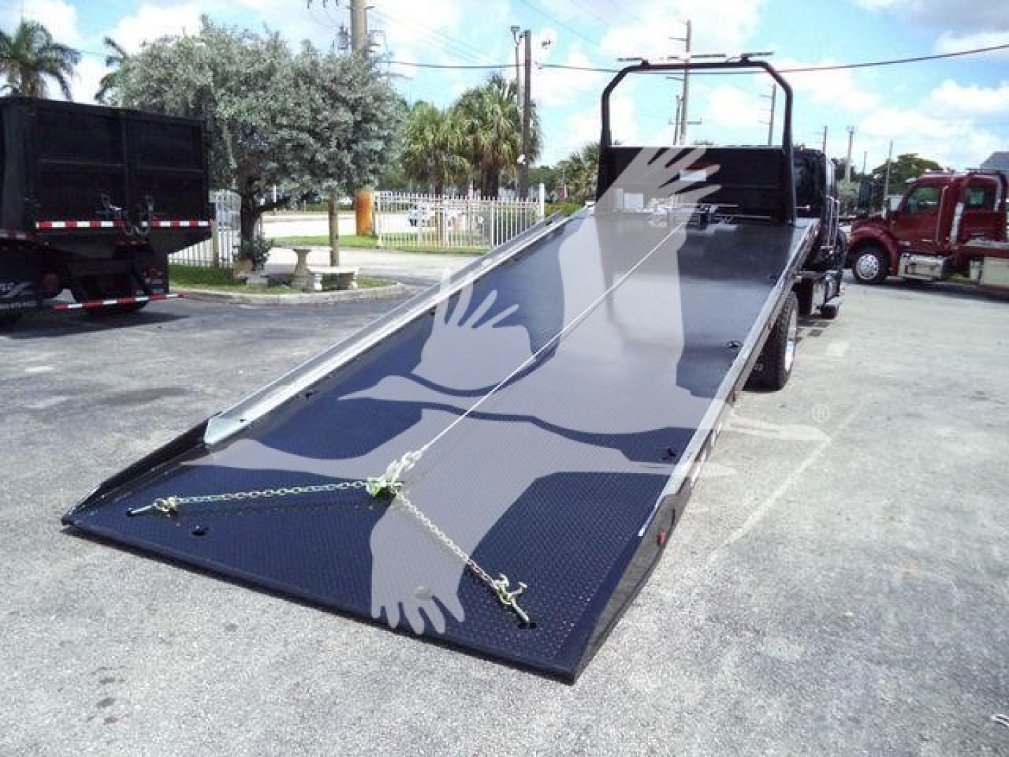 Tractor-trailer rollback truck with a flatbed tilt bed in service, showing a long blue metal ramp and rear chase area.