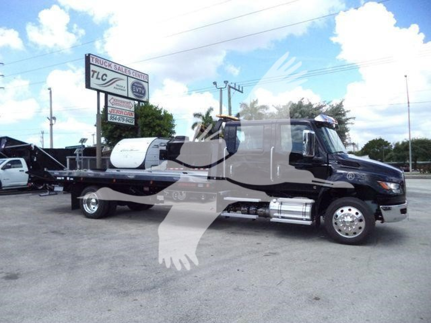 Black International MV tow truck pickup showing flatbed and chrome exhaust, side view with rollback equipment and sign in background