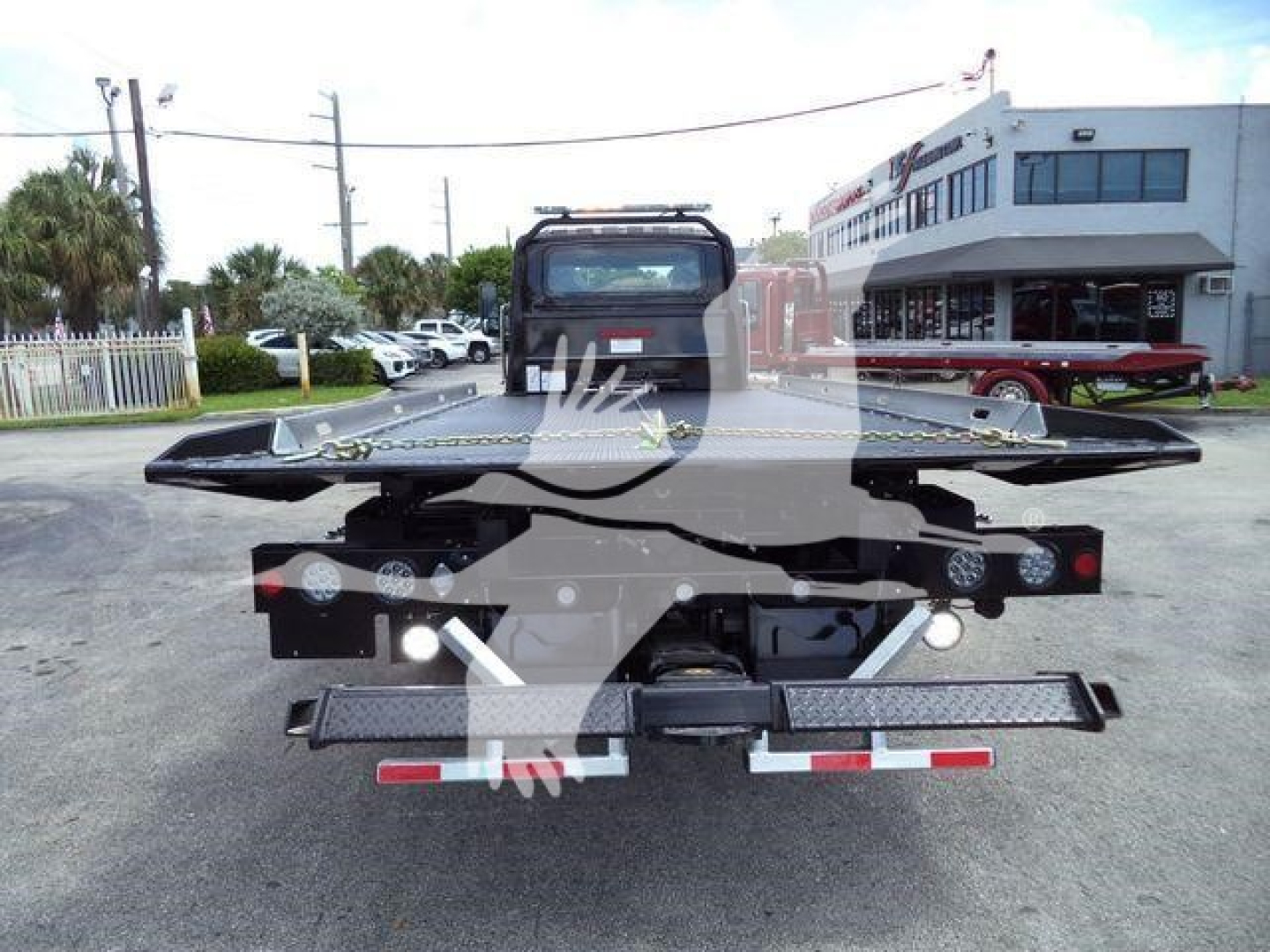 Flatbed tow truck trailer in service lot showing rear view with lights and hitch.