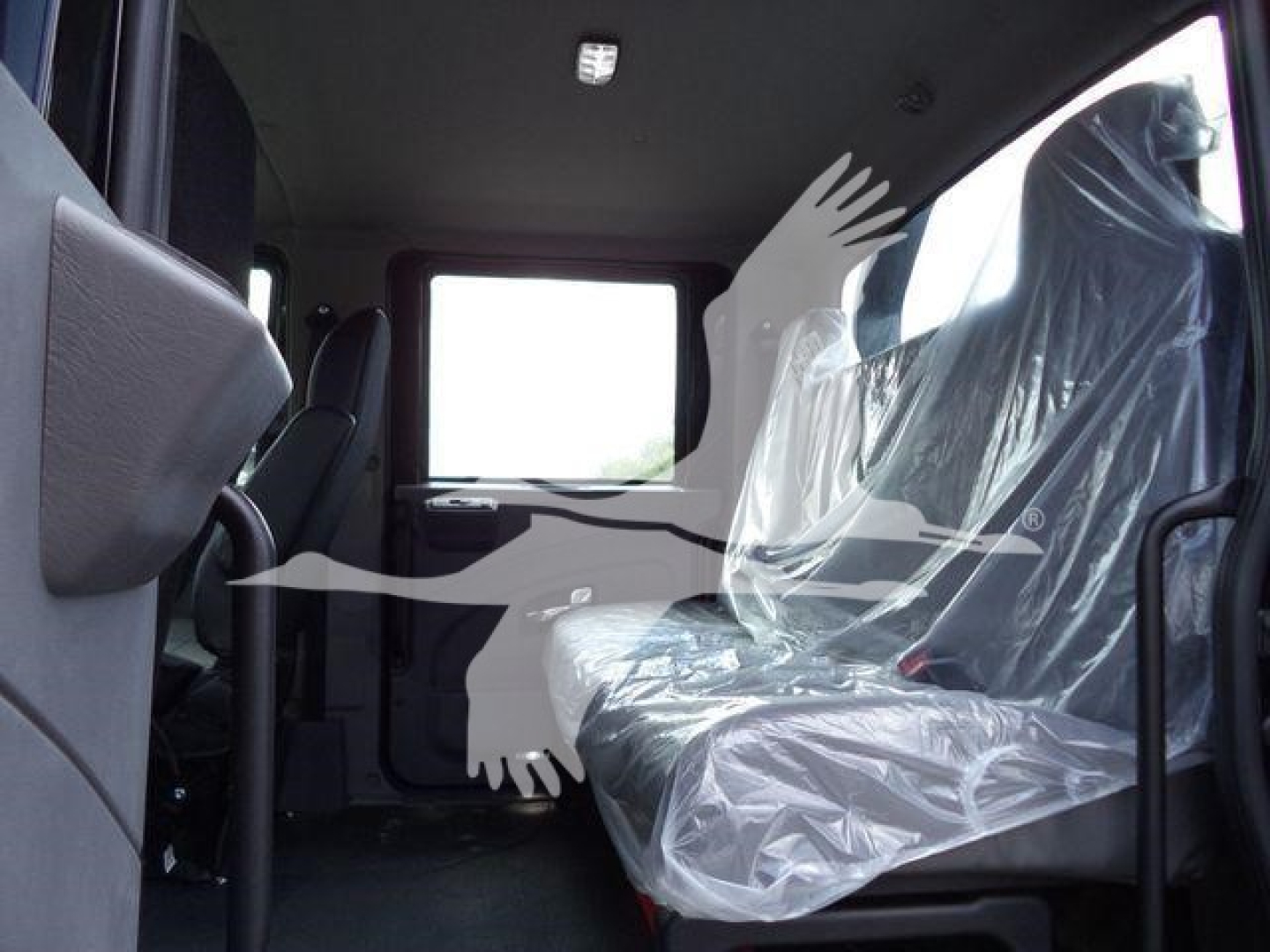 Interior of a new International MV rollback truck showing plastic-wrapped front and rear seats and wide cab door opening.