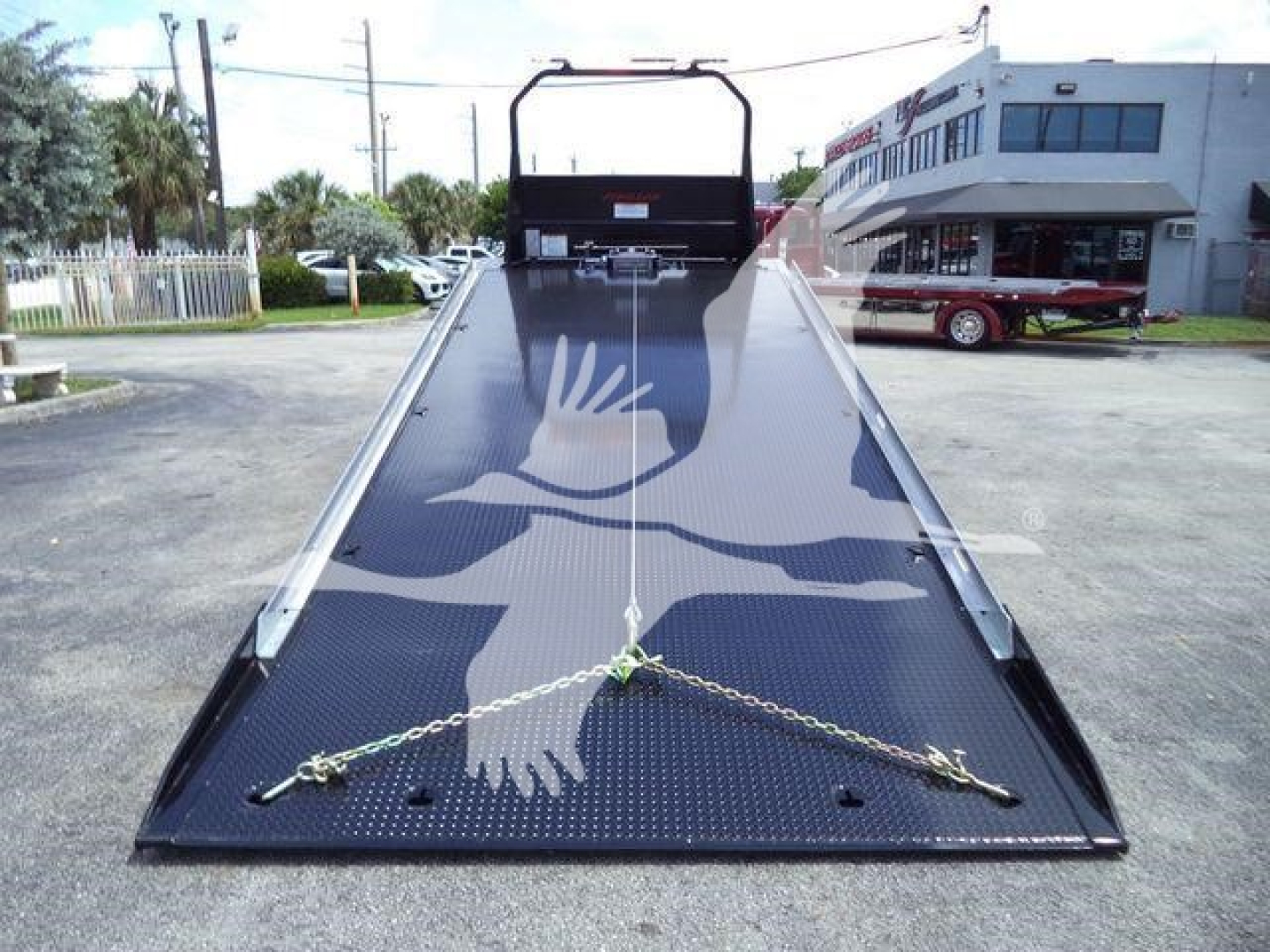 Truck rollback bed platform with black diamond-plate surface and tow chains across the ramp, International MV in background.