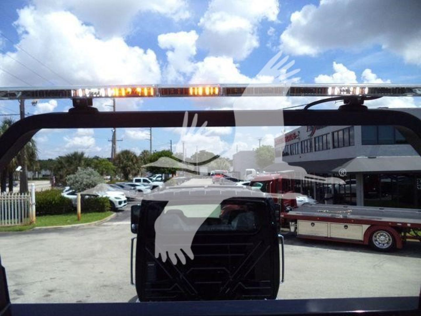 Truck rear window view showing light bar and part of emergency vehicle at a dealership lot for an International MV rollback truck.