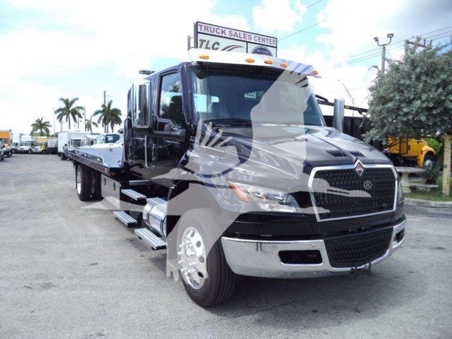 Truck bay showing 2026 International MV rollback tow truck with black body and chrome front grille, side mirrors, and flatbed.