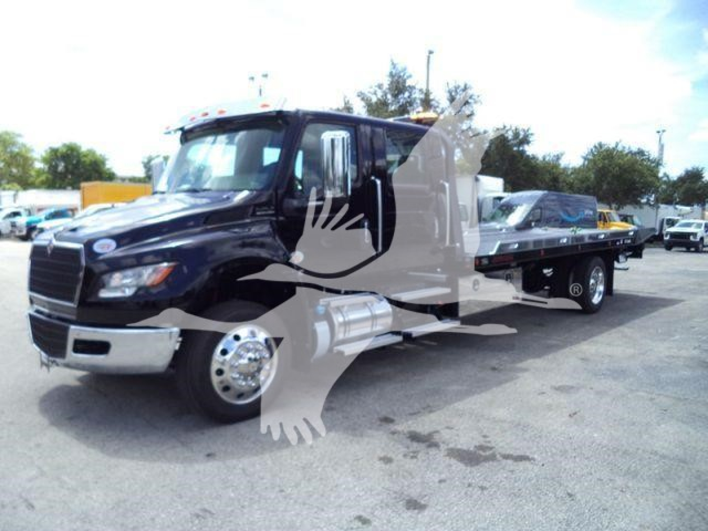 Truck cab and flatbed tow truck shown in side view with branding watermark overlay; International MV model truck in a dealership lot.