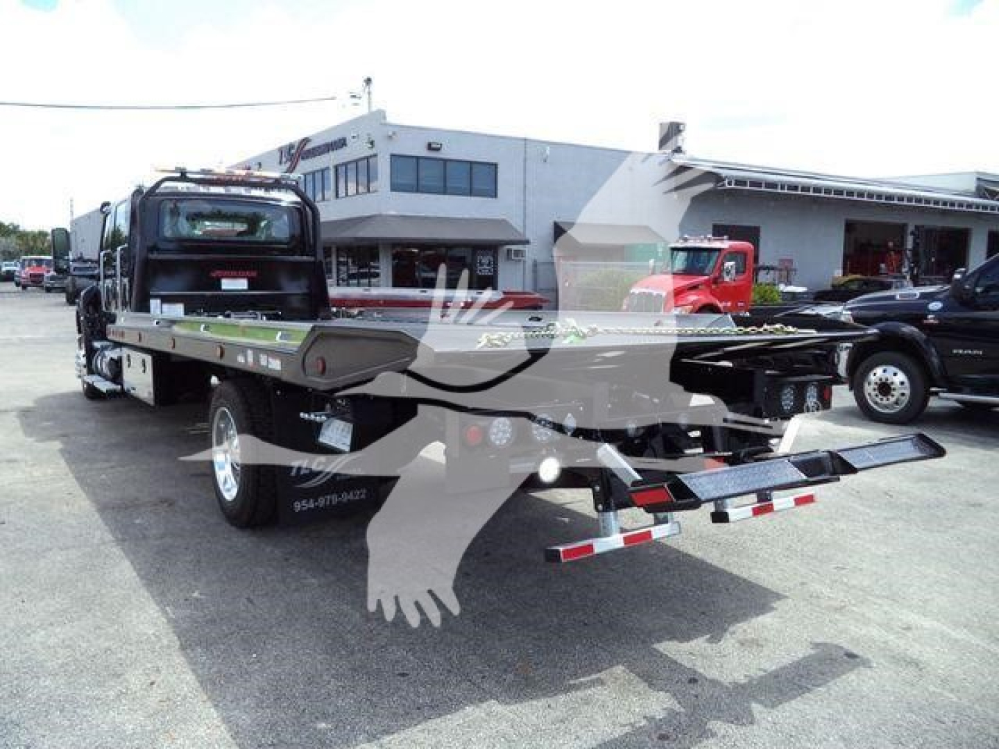 Truck rollback bed with chrome wheels and rear hitch, International MV roll-back tow truck in lot with dealership buildings in background.