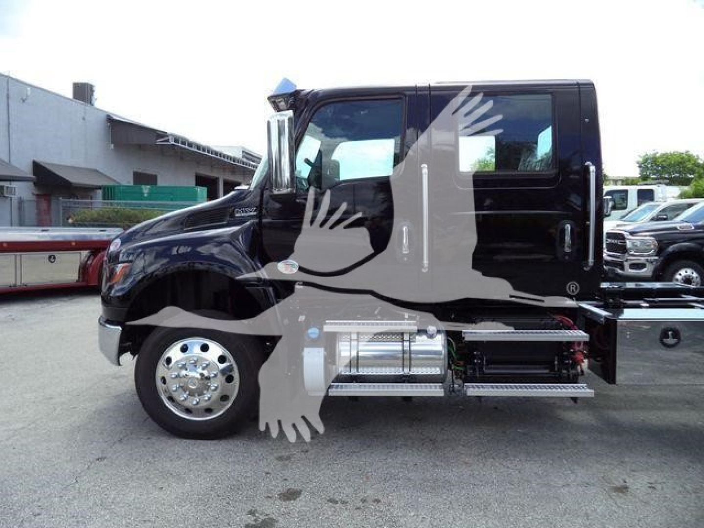 Truck cab side view showing black International MV with side steps and chrome fuel tanks. No visible text legible other than the watermark of a bird across the image.