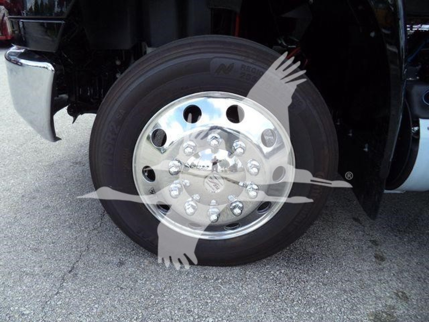 Truck wheel and chrome hub showing polished aluminum wheel with lug nuts on International MV truck, partial fender and tire visible.