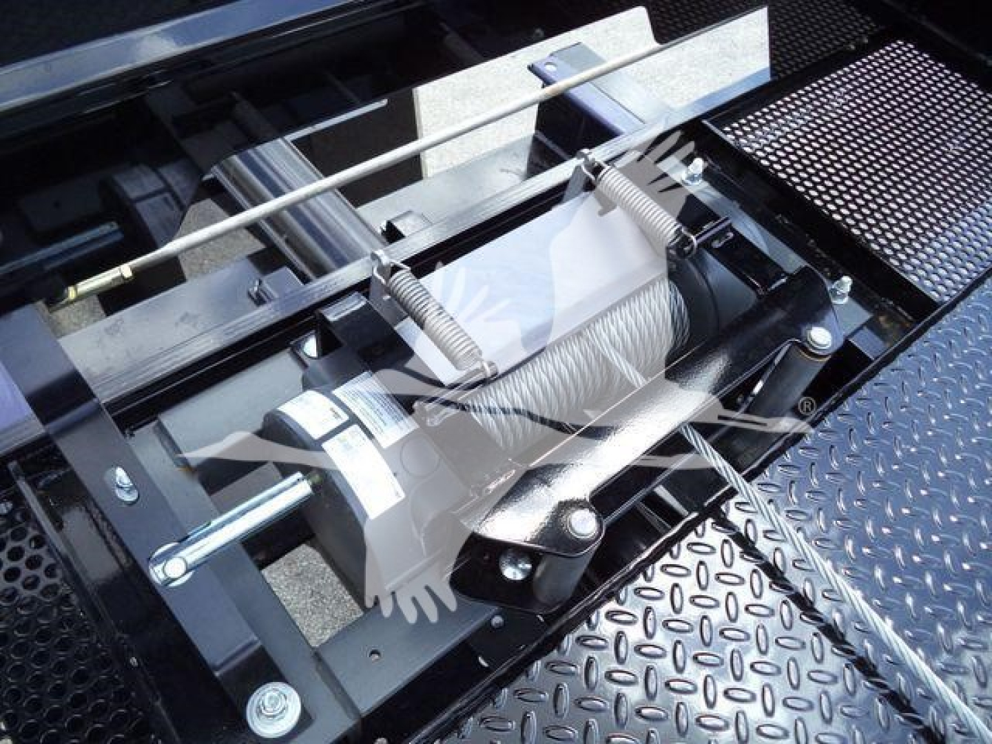 Hook winch system on rollback truck showing winch drum and steel cable with protective housing.
