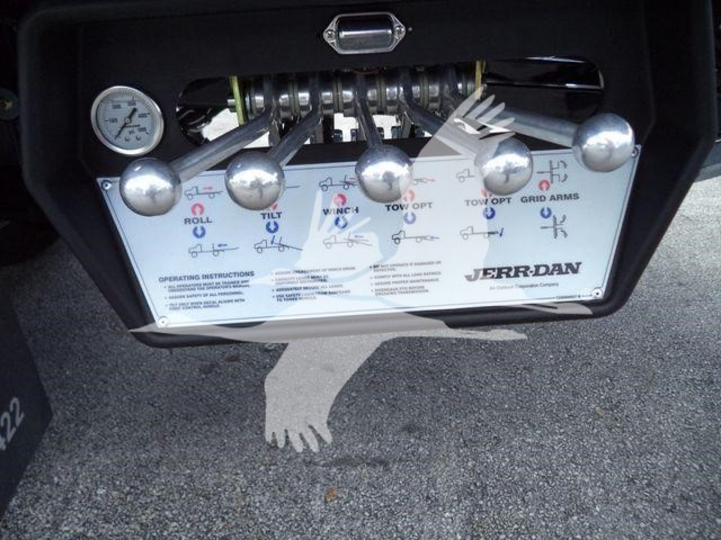 Dashboard-style control panel with levers and a gauge labeled on a JerrDan rollback tow truck. Visible labels include roll, tilt, winch, tow, grid arms with knob handles and a pressure gauge. text says JERRDAN on panel.