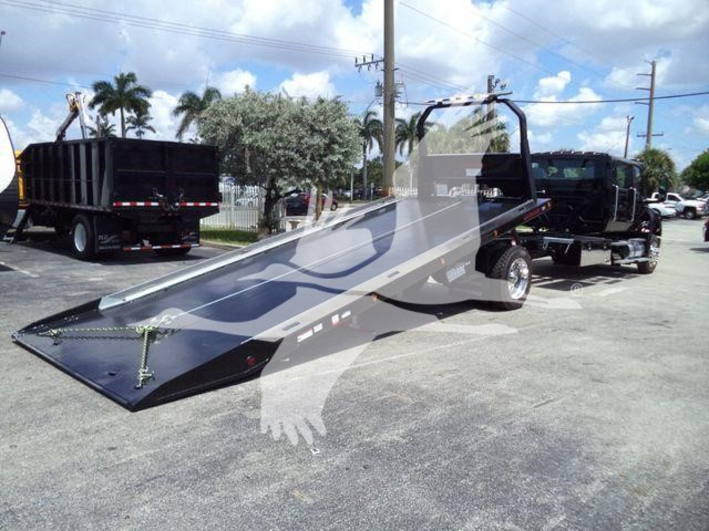 Flatbed rollback tow truck with a long inclined ramp attached to a tow truck chassis; side rails and wheel ramps; tag visibility on ramp edge.