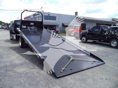 Truck bed shows a ramped rollback trailer with a black steel surface and diamond plate ramp. It has a winch line and hooks at the front, with a cab-over truck in background.