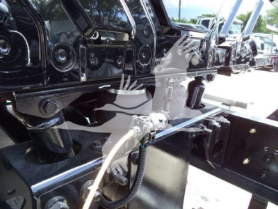 Truck chassis and undercarriage components showing frame and hitch area with hoses and wiring, MV model lineup in background.