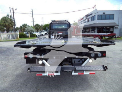 Flatbed tow truck trailer in service lot showing rear view with lights and hitch.