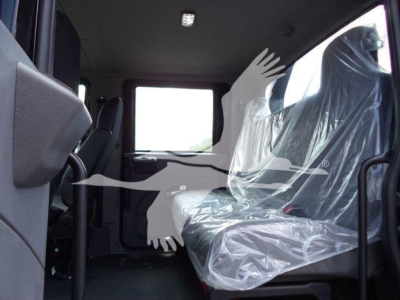 Interior of a new International MV rollback truck showing plastic-wrapped front and rear seats and wide cab door opening.