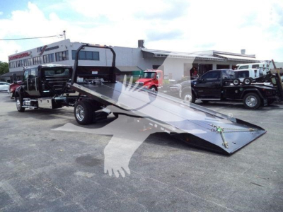 Tilt-bed tow truck with a ramp in a dealership lot; faint watermark overlay from listing. No legible model text clearly visible on vehicle.