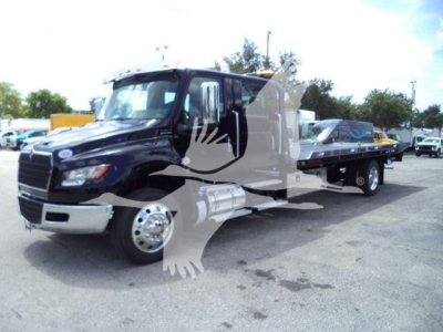 Truck cab and flatbed tow truck shown in side view with branding watermark overlay; International MV model truck in a dealership lot.