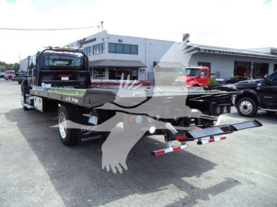 Truck rollback bed with chrome wheels and rear hitch, International MV roll-back tow truck in lot with dealership buildings in background.