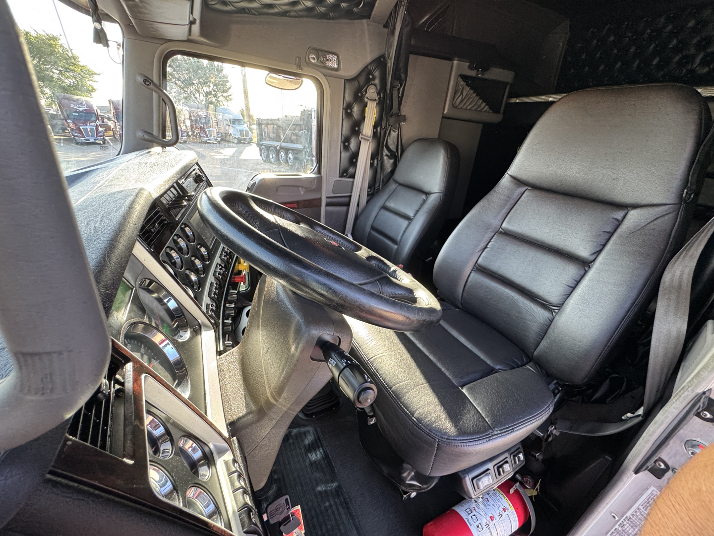 Kenworth W900L cab interior showing steering wheel and driver's seat with dashboard controls and window view.
