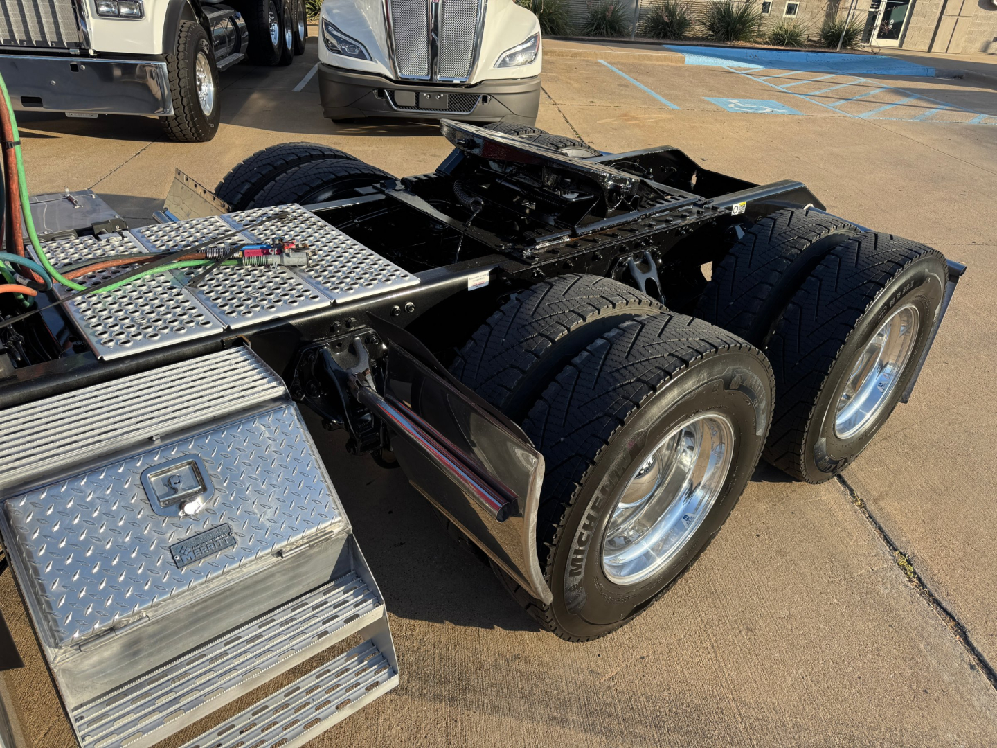 Kenworth W900L truck chassis showing rear dual tandem wheels and fuel/utility steps with diamond plate surfaces.