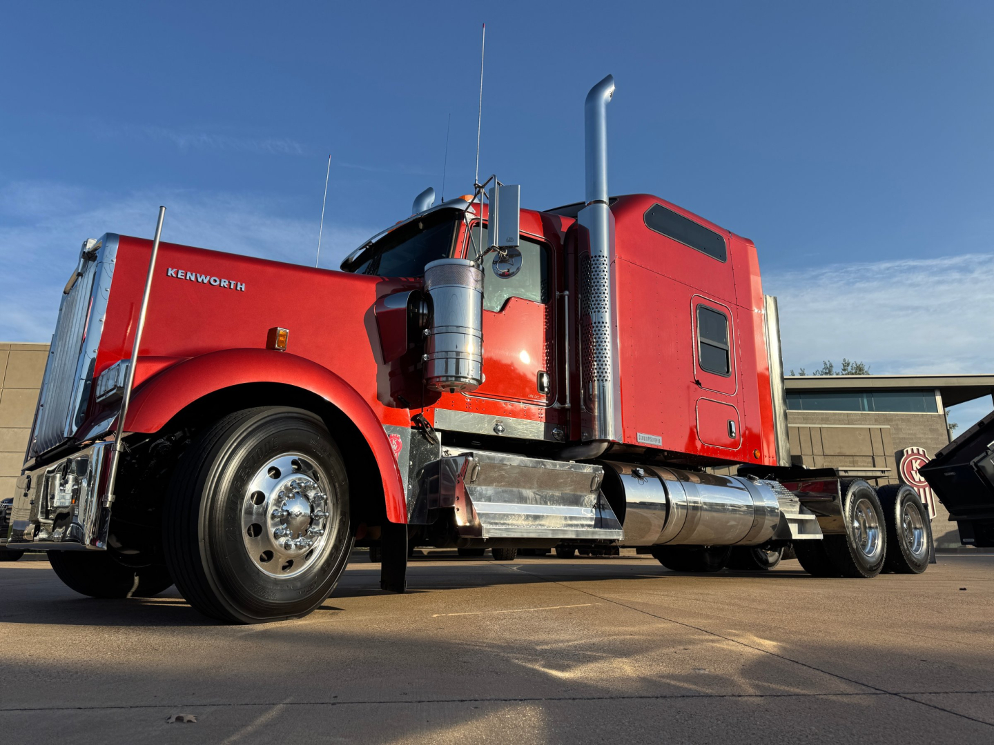 Kenworth W900L conventional sleeper truck side view with red cab and chrome fuel tanks, dual rear axles, and long wheelbase.