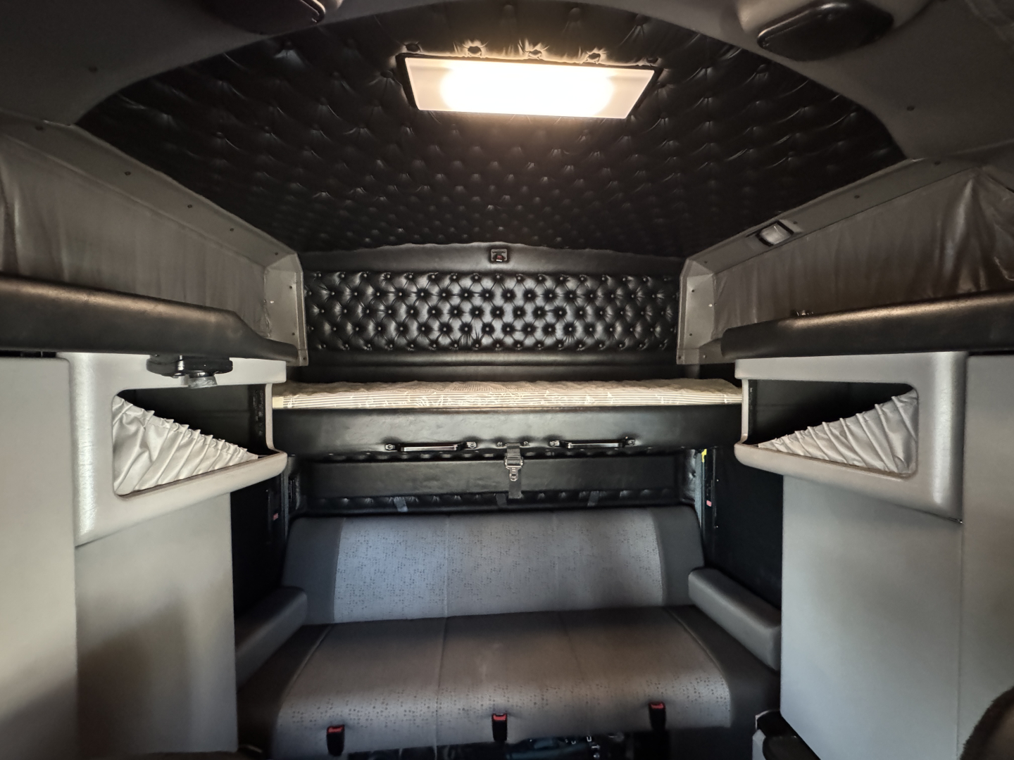 Kenworth W900L sleeper cab interior showing bunk beds and storage cabinets with quilted black headliner.