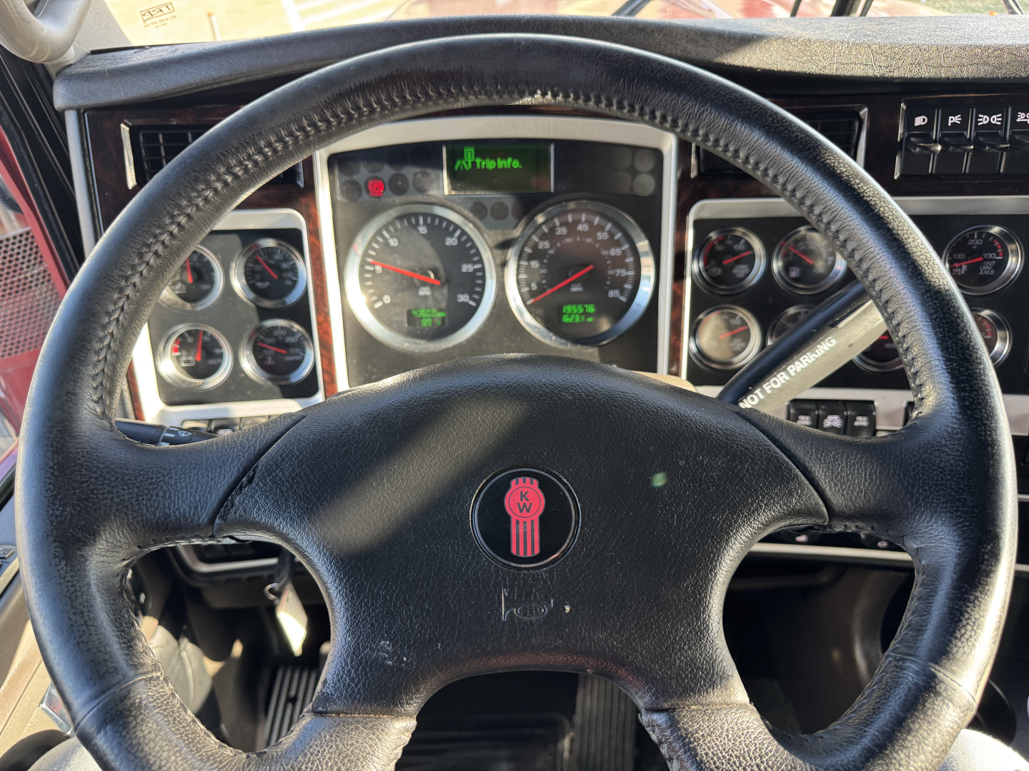 Kenworth W900L interior view of steering wheel and dashboard gauges; steering wheel center features KW emblem; multiple analog gauges visible