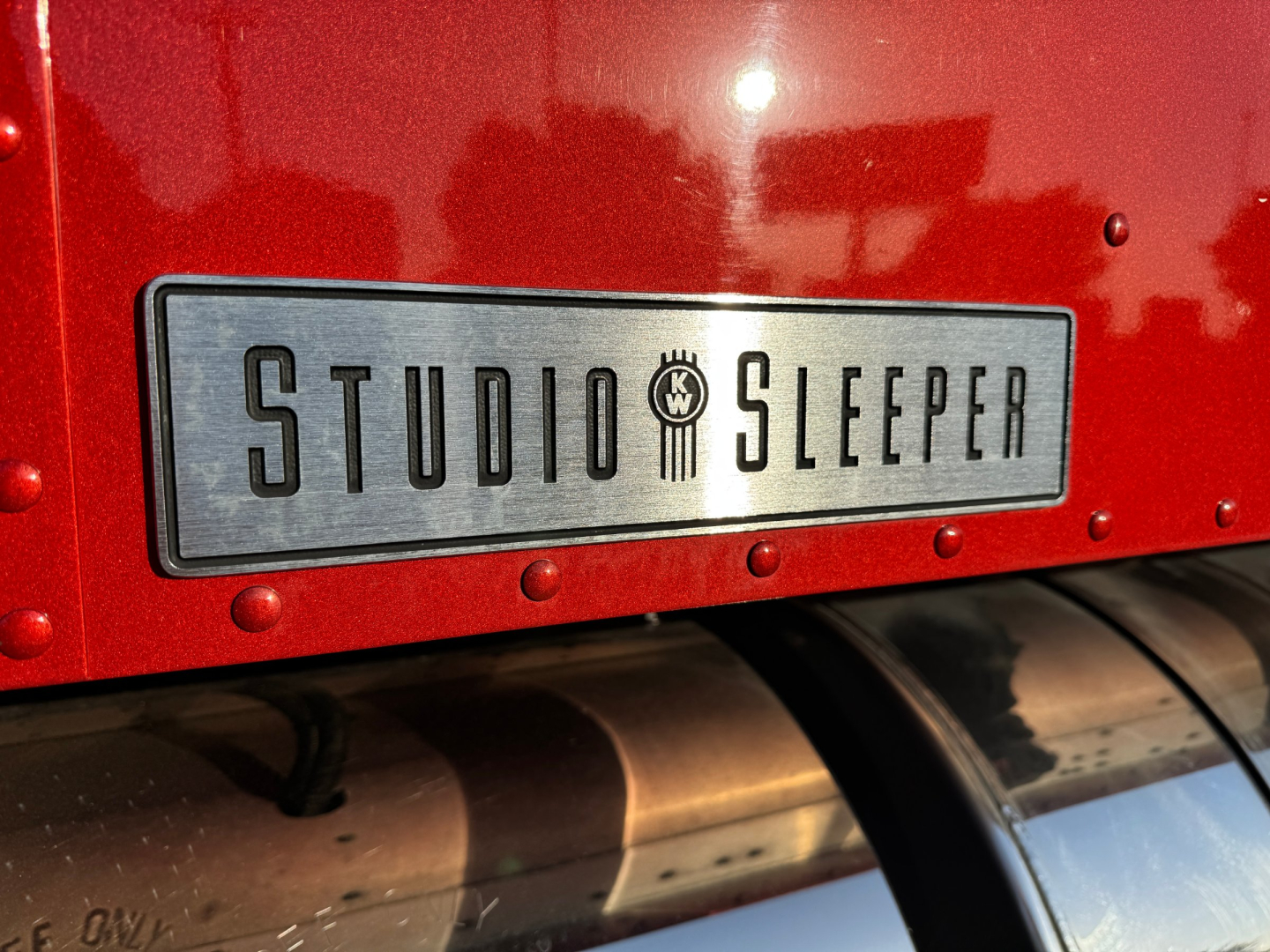 Kenworth W900L truck rear with Studio Sleeper badge plate and red paint visible.