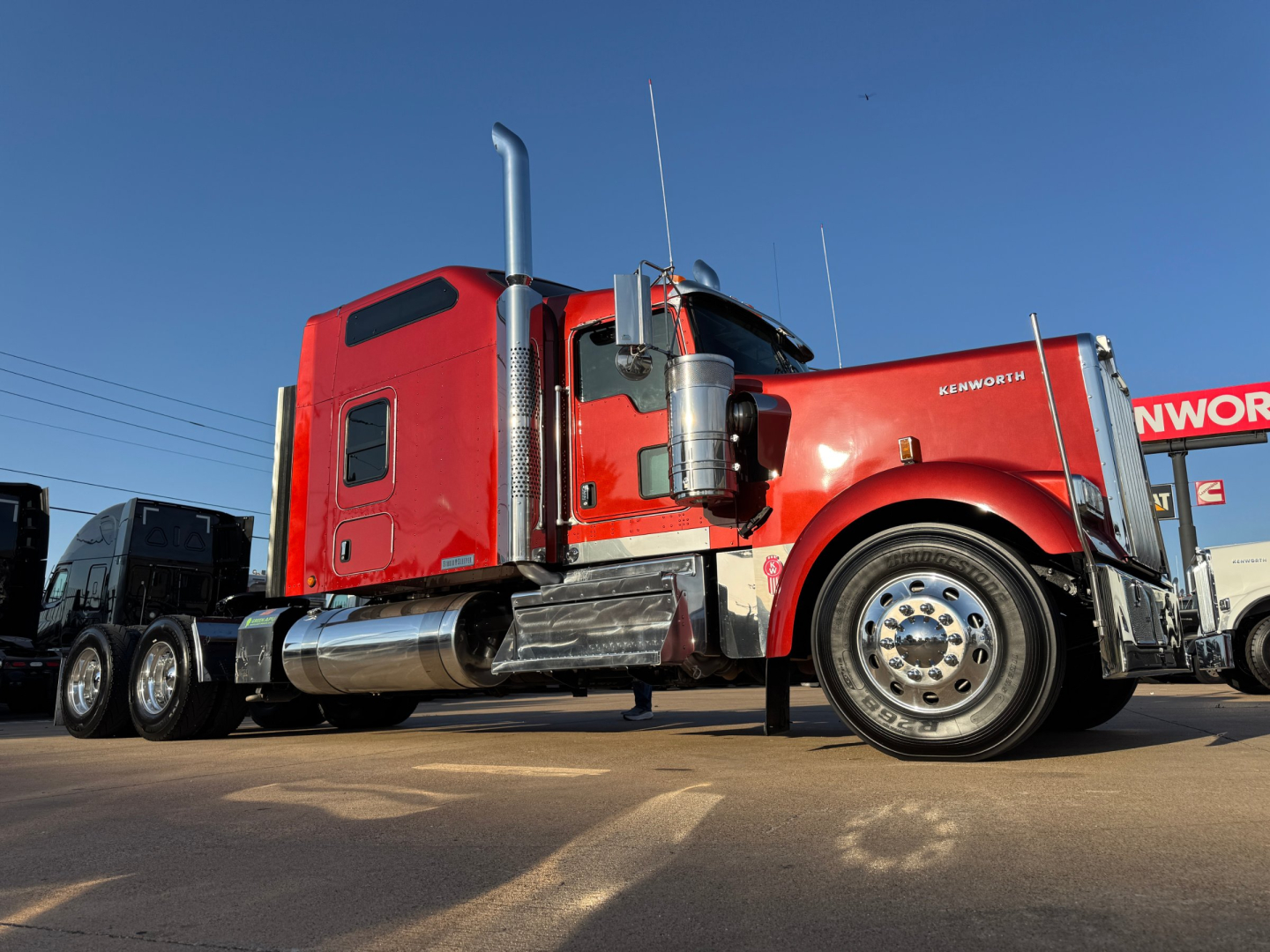 Kenworth W900L conventional sleeper truck in red, side view showing chrome fuel tanks and front wheel with hubcap.