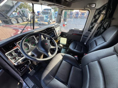 Truck cab interior of a 2025 Kenworth W900L showing steering wheel, dashboard, and driver seat; visible instrumentation and control panels.