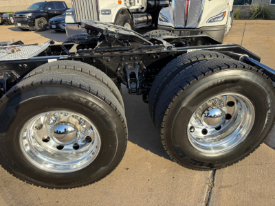 Kenworth W900L truck chassis showing dual rear axles with chrome wheels and tires, fuel tank, and frame in view.
