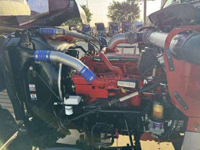 Truck engine bay showing red engine, intercooler hoses with blue clamps, radiator, hydraulic reservoir, and various components in a Kenworth W900L.