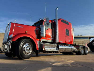 Kenworth W900L conventional sleeper truck side view with red cab and chrome fuel tanks, dual rear axles, and long wheelbase.